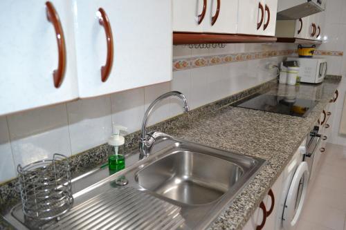 una cocina con fregadero de acero inoxidable y armarios blancos en Vivienda Falda del Monsacro, 