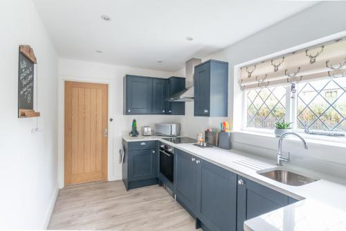 a kitchen with blue cabinets and a sink and a window at Luxury cosy cottage, enchanting forest location. in Ringwood