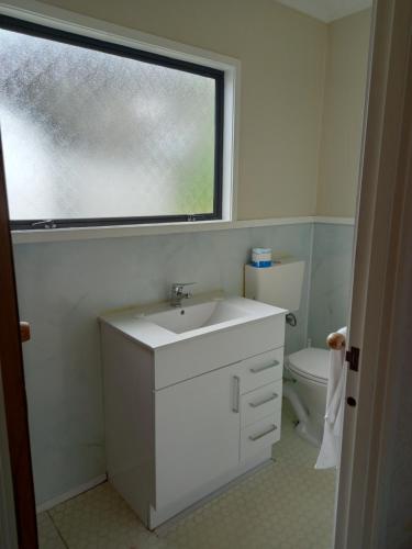 ein weißes Bad mit einem Waschbecken und einem Fenster in der Unterkunft Pinelodge in Opua