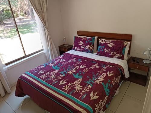 a bedroom with a bed with a purple comforter and a window at Cabaña El Tiempo Es Arte in San José de Maipo