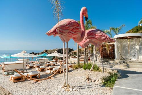 two pink flamingos on a beach with lounge chairs at Folie Marine Hotel & Beach Club in Jal