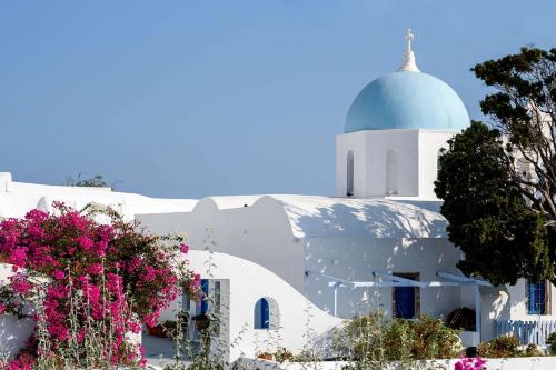 a white building with a dome on top with pink flowers at Aghios Artemios Traditional Houses in Imerovigli