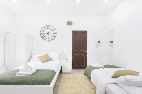 two beds in a white room with a clock on the wall at Beautiful Studio Flat in Hackney next to Overground Station in London