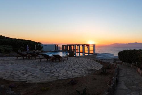 a sunset on a patio with a table and benches at Aegean Stones in Agios Ioannis Mykonos