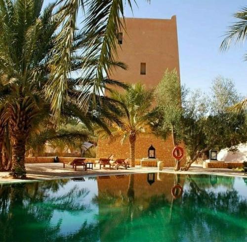 a swimming pool in front of a building with palm trees at Hotel Pansy in Ksar Ghilane