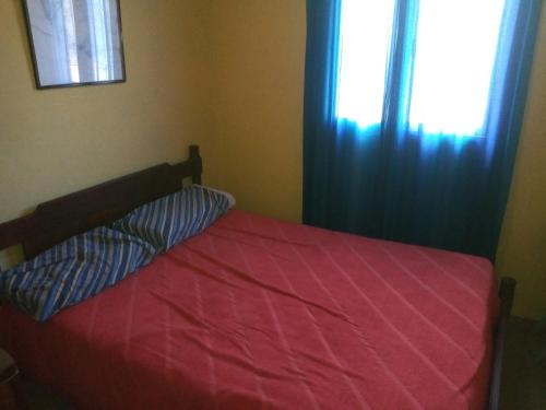 a bed with a red comforter and a window at La Griselda in El Mollar