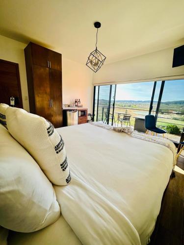 a bedroom with a large white bed with a large window at Siempre Valle Hotel Boutique in Valle de Guadalupe