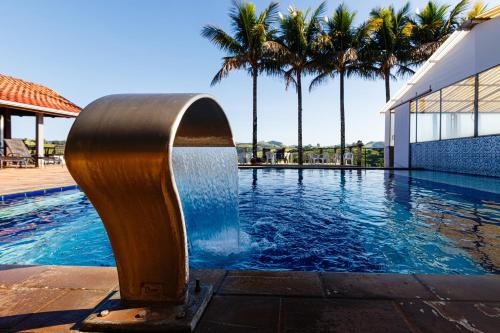 a fountain in front of a swimming pool with palm trees at Hotel Morro De Santo Agostinho in Serra Negra