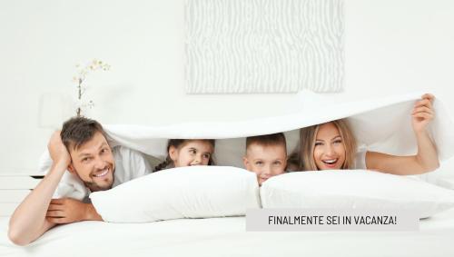 una famiglia sdraiata sul letto sotto un lenzuolo di Hotel B&B Ardea Rimini a Rimini