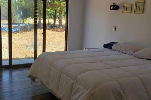 a bed in a bedroom with a large window at Casa en condominio de parcelas in Yumbel