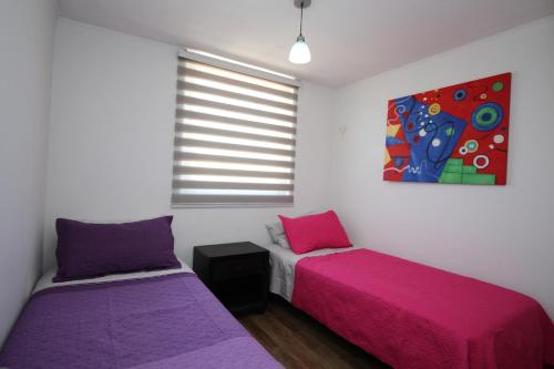 2 camas en una habitación con sábanas rosas y moradas en Departamento Edificio Terrazas de Sol, en La Serena