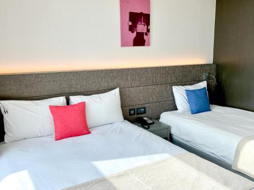 two beds in a hotel room with red and blue pillows at Airsky Hotel Incheon in Incheon
