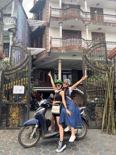 two women sitting on a scooter in front of a building at Nam Phương Riverside Villa in Hue