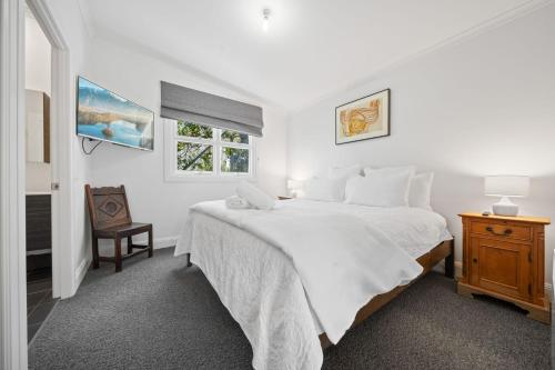 a white bedroom with a large bed and a window at Tukidale Cottage - 3BR Cottage l WiFi l Air-Con l Relaxing Location in Crackenback