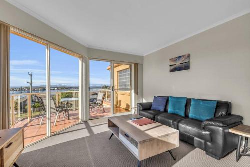 a living room with a black leather couch and a balcony at Baywatch - Unit 6 in Merimbula