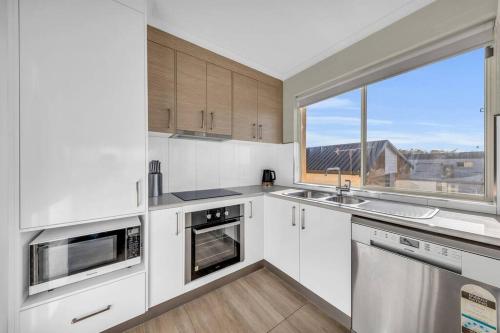 a kitchen with white cabinets and a large window at Baywatch - Unit 6 in Merimbula