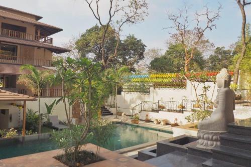 a resort with a pool and a statue next to a building at Anamiva, Goa - AM Hotel Kollection in Anjuna