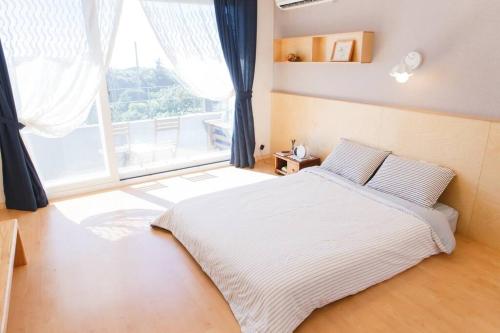 a bedroom with a white bed and a large window at PREERIA Pension in JEJU in Jeju