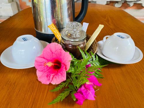 a table with two white plates and a pink flower at Aura Bisma Guesthouse in Ubud