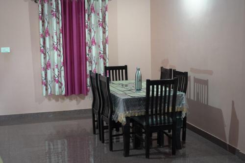 a dining room table with four chairs and a glass vase at Coorg Stream Side Homestay in Ponnampet