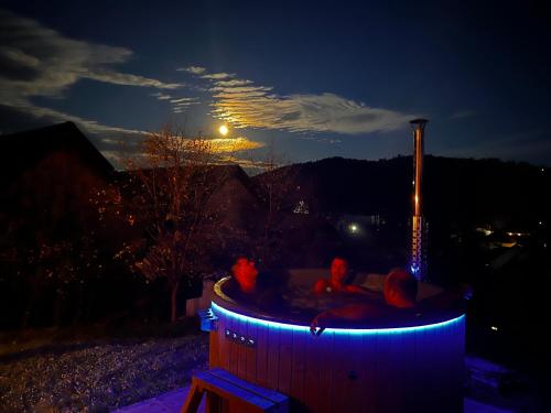 3 persone sedute in una vasca idromassaggio di notte di Bucovina Lodge Pension a Vama