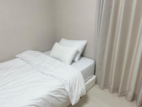 a white bed with two pillows sitting next to a window at Landmark Stay in Songdo in Incheon