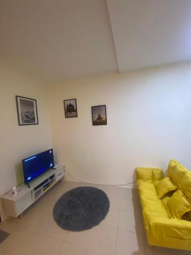 a living room with a yellow couch and a tv at Cozy 2-BR in UDH, Manila in Manila