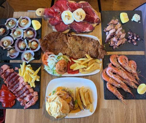 une table en bois recouverte de plaques de viande et d'autres denrées alimentaires dans l'établissement Hostal Julio Cesar, à La Virgen del Camino