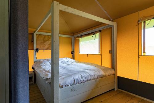 a bedroom with a canopy bed in a room with yellow walls at Luxe Safaritent 6 persoons op Camping Rijsterbos in Rijs