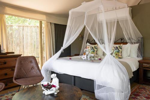 a bedroom with a canopy bed and a chair at Umkumbe Bush Lodge - Luxury Tented Camp in Skukuza