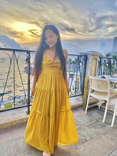 a woman in a yellow dress standing on a balcony at Sea Sunset Hotel Phu Quoc - Welcome to a mixing world of friends in Phu Quoc
