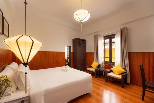 a bedroom with a large white bed and two chairs at Hoianese Heritage Hotel - Truly Hoi An in Hoi An