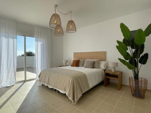 a white bedroom with a bed and a potted plant at Villa con piscina privada y AC in Sant Lluis
