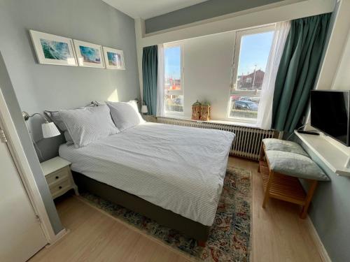 a small bedroom with a bed and two windows at Strandzicht Zandvoort in Zandvoort