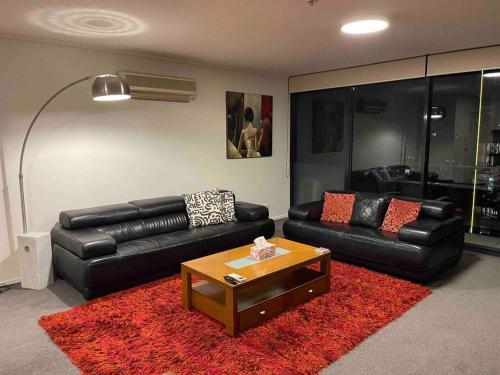 a living room with black leather couches and a red rug at Spacious 3 Bedroom Apartment Southbank in Melbourne