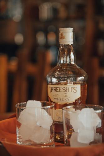 a bottle of three ships whiskey next to two glasses at Africa Awaits Lodge & Safaris in Gobabis