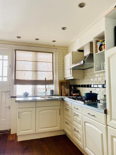 a kitchen with white cabinets and a sink and a window at Familiehuis aan zee met ruim dakterras in Zandvoort