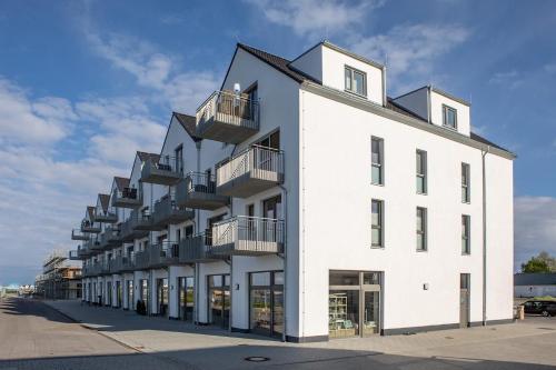 Biały budynek z balkonami na boku w obiekcie Fewo Reeder's Nest by Seeblick Ferien ORO, 2-Zi-Hafenwohnung w mieście Olpenitz