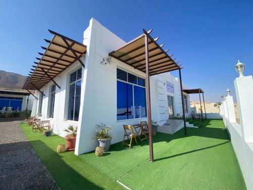 a white house with a green yard with chairs at Wadi shab guest house in Ţīwī