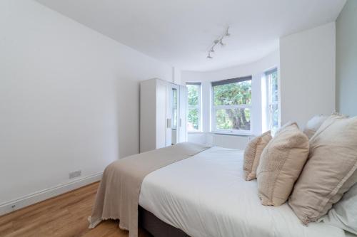 a white bedroom with a bed with pillows and a window at The Wood Green Collection in London