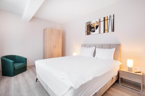 - une chambre avec un grand lit blanc et une chaise verte dans l'établissement Blissful Haven Flats, à Oradea