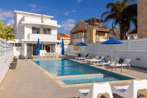 a swimming pool with chairs and umbrellas next to a house at Faros Seaside Villa Larnaca in Perivolia