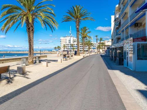 une rue sur la plage avec des palmiers et des bâtiments dans l'établissement Appartement 2P avec terrasse, garage, 250m plage, 4 pers, WiFi optionnel - FR-1-307-165, au Grau-du-Roi