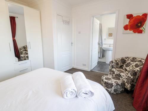 a white bedroom with a bed and a chair at Halcyon in Moelfre