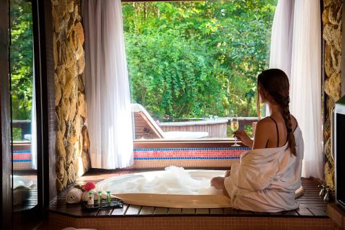 a woman sitting in a bath tub looking out a window at Maua Brasil Hotelaria in Visconde De Maua
