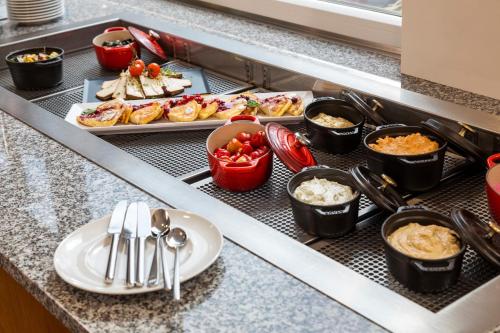 a buffet line with dishes of food on a counter at Hotel Zeitgeist Vienna Hauptbahnhof in Vienna