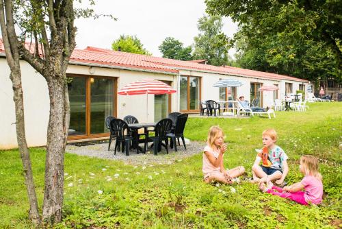 three children sitting in the grass in front of a house at Camping la Colline in Virton