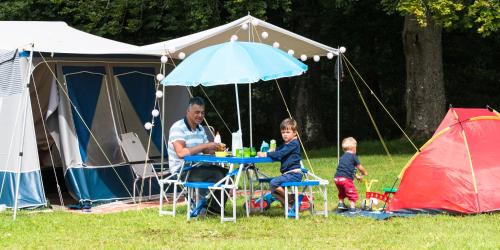 mężczyzna i dziecko siedzący przy stole przed namiotem w obiekcie Camping la Colline w mieście Virton