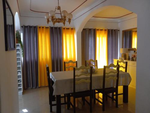 a dining room with a table and chairs and yellow curtains at Chez Leonilde in São Filipe