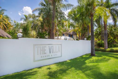 a sign on a white wall with palm trees at The Villa Manor & Spa in Bela-Bela